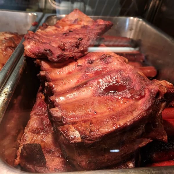 Close-up of Roy's Hickory Pit BBQ ribs, glistening with sauce in a metal tray.