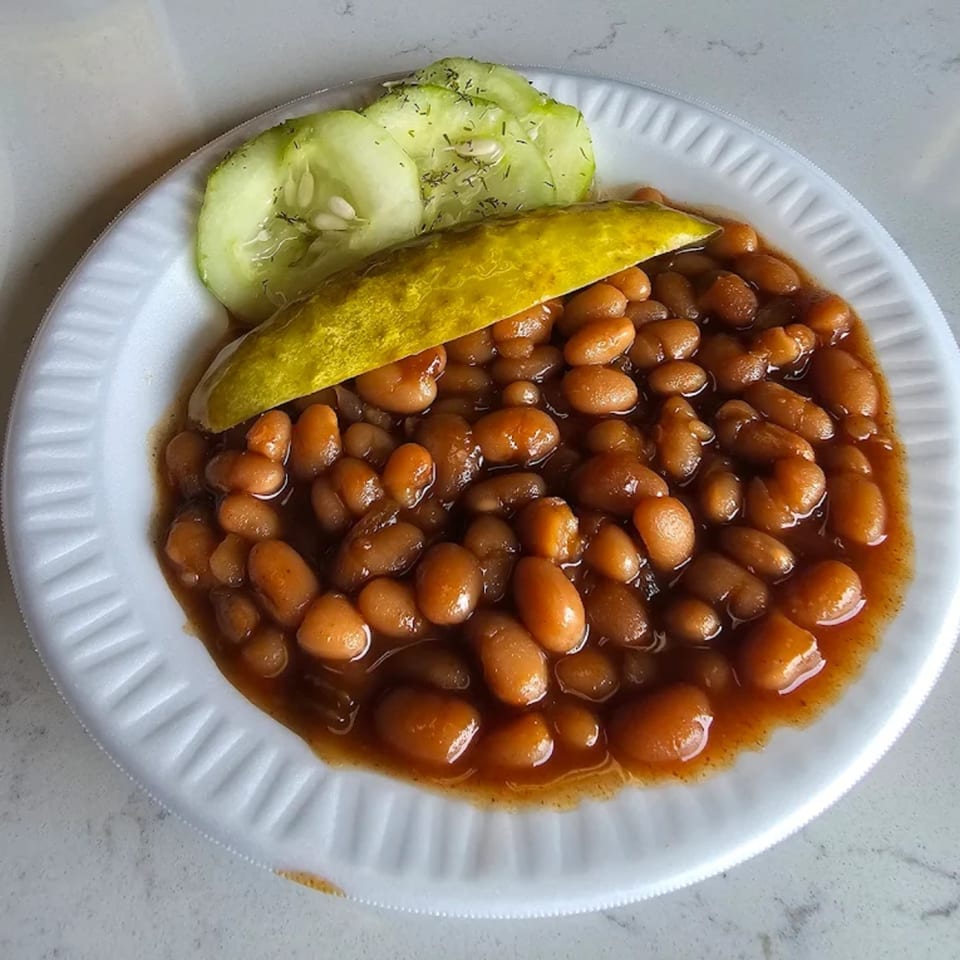 Roy's Hickory Pit BBQ baked beans with a pickle spear and cucumber slices on a white plate.