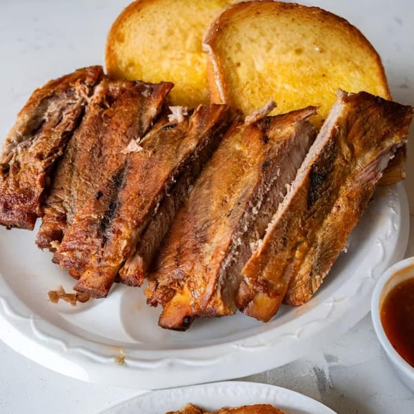 Roy's Hickory Pit BBQ ribs and Texas toast on a white plate with a side of sauce.