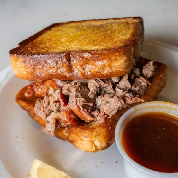 Roy's Hickory Pit BBQ's pulled pork sandwich on toasted bread with a side of BBQ sauce.