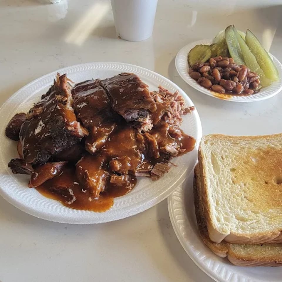 Roy's Hickory Pit BBQ plate with saucy ribs, pulled pork, baked beans, pickles, and toast.