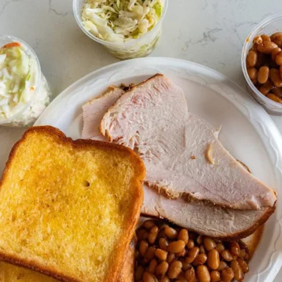 A Roy's Hickory Pit BBQ plate with sliced turkey, baked beans, Texas toast, and coleslaw.